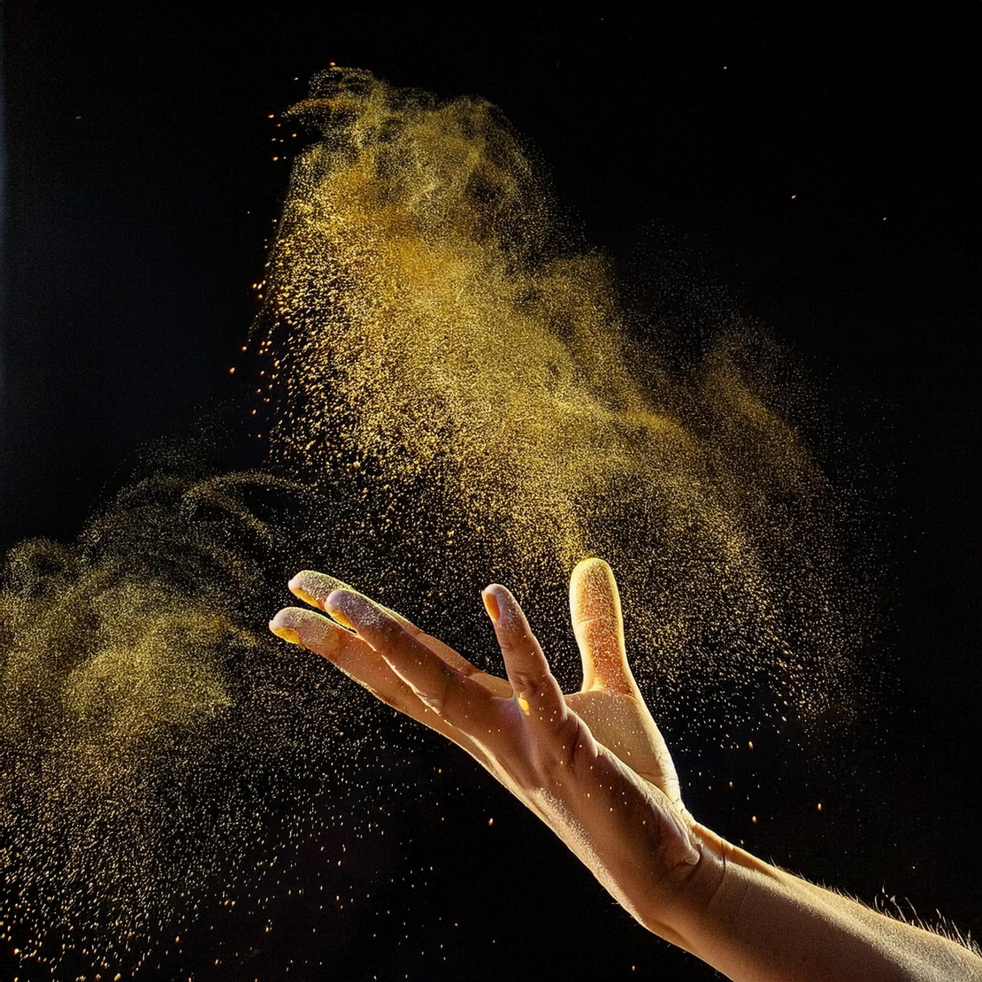 A open feminine hand throwing golden dust into the air with a black background
