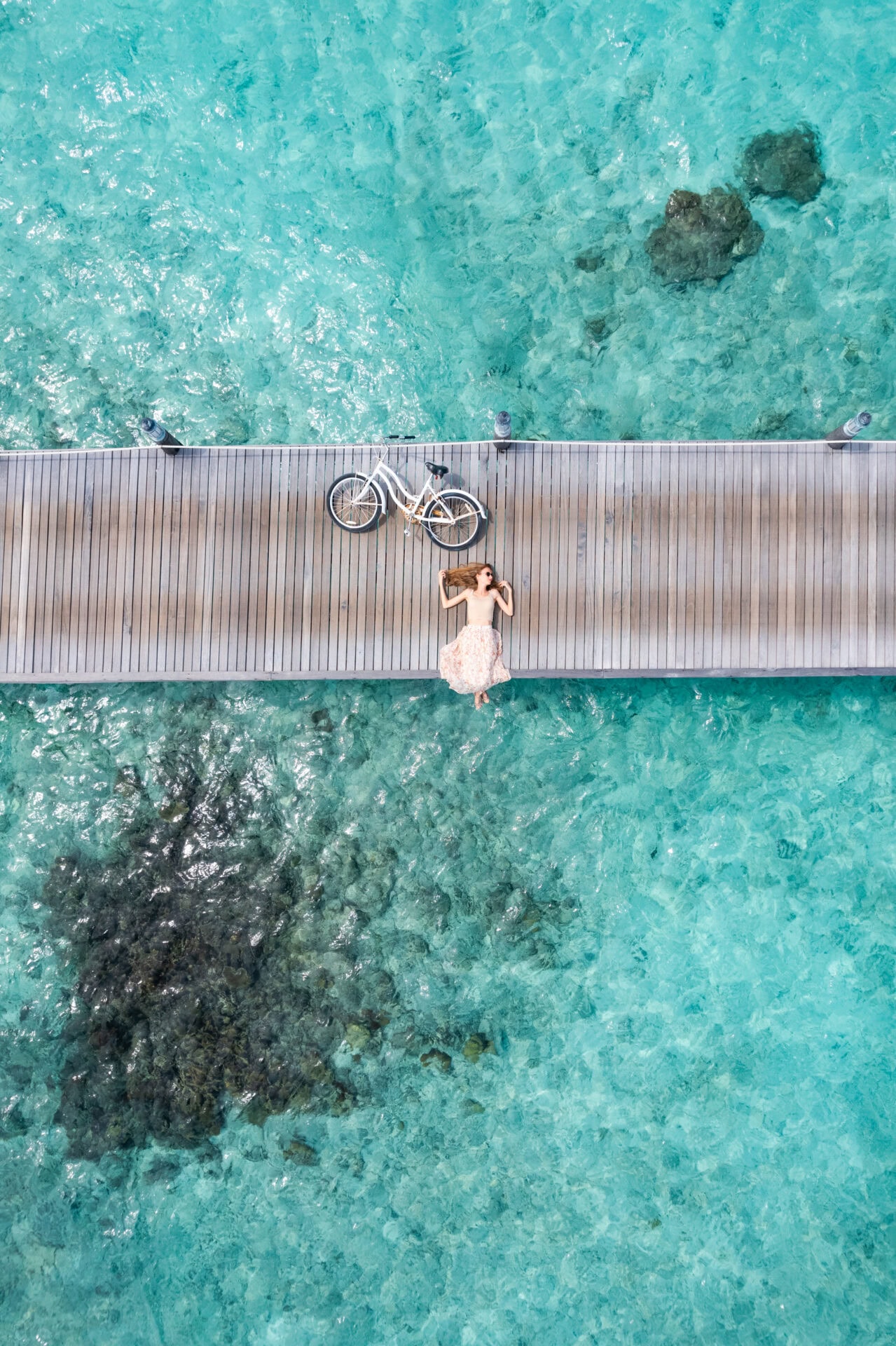 Beautiful woman lying down on jetty with bicycle in Maldives