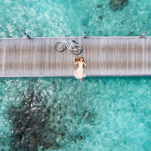 Beautiful woman lying down on jetty with bicycle in Maldives